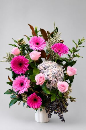 A beautiful mixed arrangement of seasonal roses, gerberas, hydrangea, and premium foliage, elegantly presented in a ceramic vase